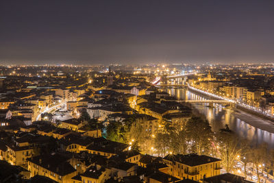 Illuminated cityscape by adige river against sky at night