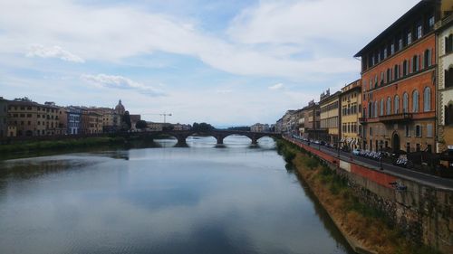 Arch bridge over canal amidst buildings in city against sky