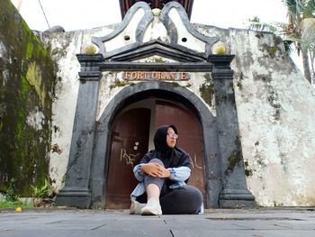 Low angle view of woman sitting against house