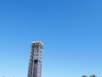Low angle view of crane by building against clear blue sky