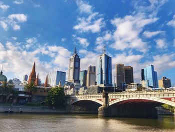 Bridge over river by buildings against sky in city