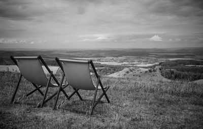 Deck chairs on field against sky