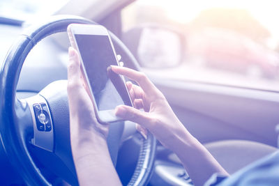 Cropped hand of woman using mobile phone in car