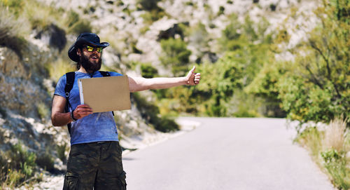 Man asking hitchhiking while holding blank cardboard on road