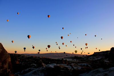 Hot air balloons flying over rocks against sky during sunset