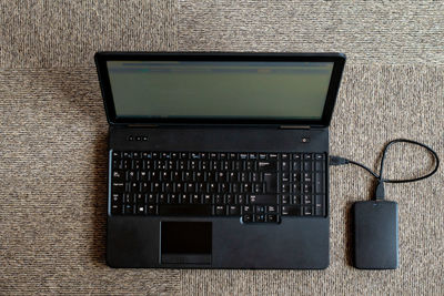 Directly above shot of laptop connected to hard drive on carpet