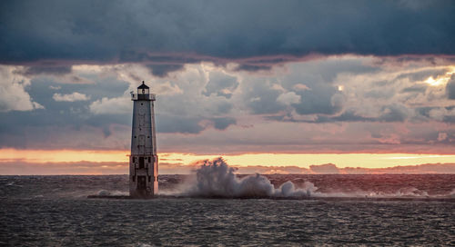 Lighthouse by sea against sky during sunset