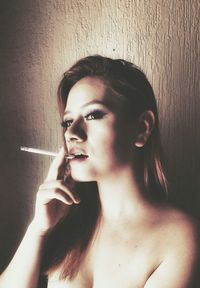 Close-up of sensuous naked woman smoking cigarette against wall