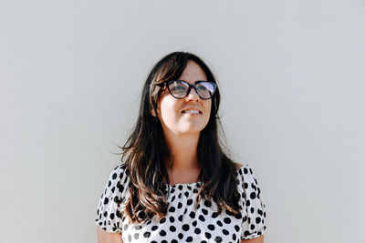 Portrait of a beautiful young woman with eyeglasses against solid grey background.