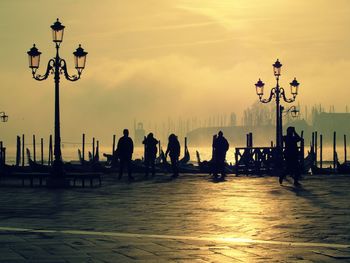 Silhouette people on sea against sky during sunset