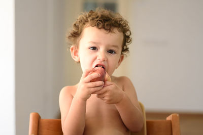 Portrait of cute baby girl eating fruit at home