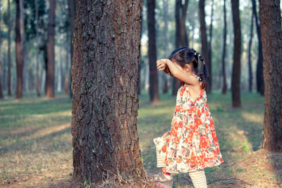 Side view of girl standing in front of tree trunk at forest