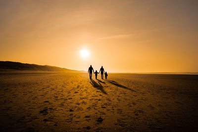 Silhouette people on shore against sky during sunset