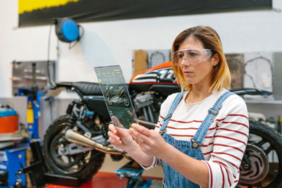 Female mechanic using transparent digital tablet with motorcycle diagnosis app