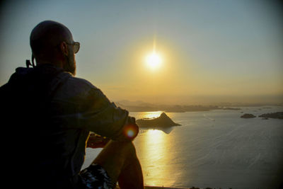 Rear view of man looking at sea against sky during sunset