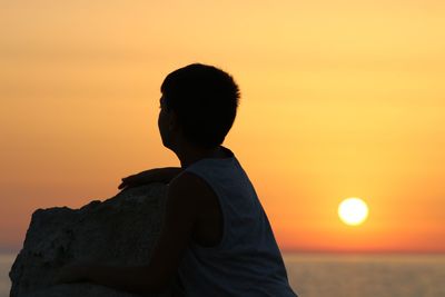 Rear view of silhouette man standing on rock at sunset