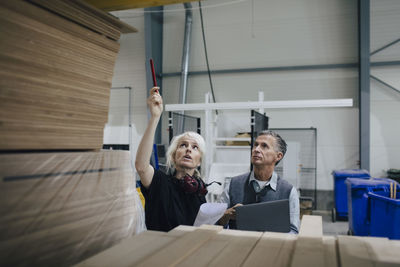 Mature woman discussing with colleague while examining wooden planks at industry