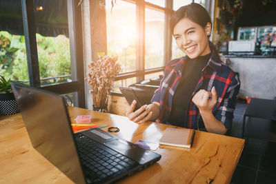 Young woman using mobile phone while sitting on table