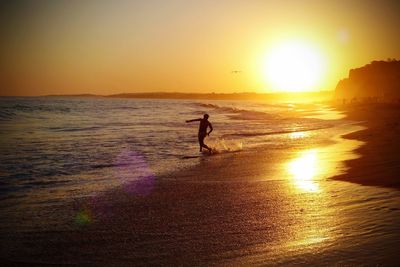 Silhouette person on beach against sky during sunset