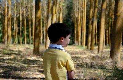Boy standing against trees in forest