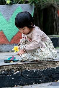 Cute girl playing with flower by flip-flop on footpath 