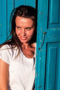 Young woman looking away while standing by blue door