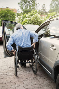 Rear view of man in wheelchair outside car