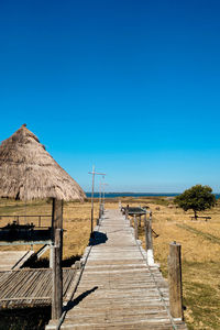 Boardwalk leading towards sea against clear blue sky