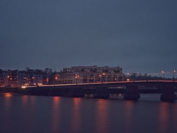 Illuminated city by river against sky at night