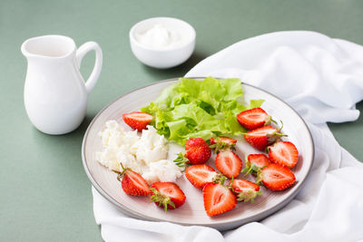 Fresh whole and sliced strawberries, cottage cheese and lettuce on a plate and sour cream in a bowl 