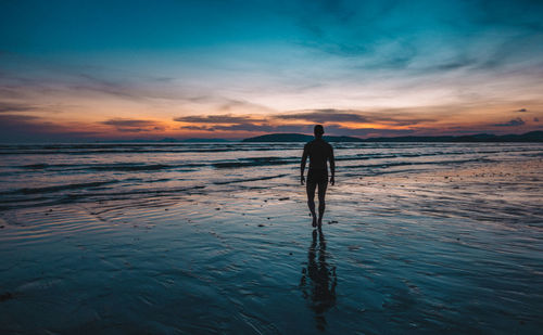 Silhouette man walking on shore at beach against sky during sunset