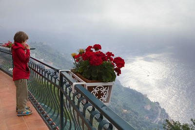 Rear view of woman standing by railing on mountain against sky