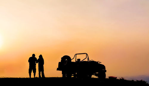 Silhouette friends with car on field against clear sky during sunset