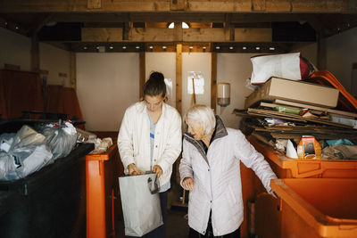 Elderly woman and female healthcare worker peeking into bag at storage room