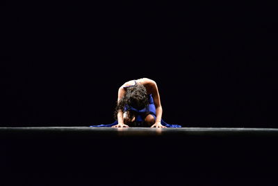 Woman kneeling on floor against black background