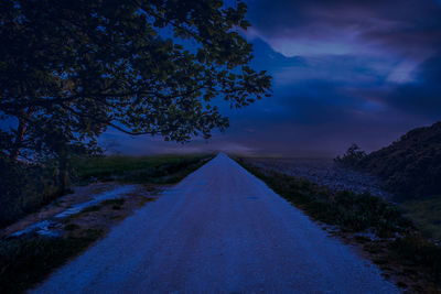 Road amidst trees against sky at dusk