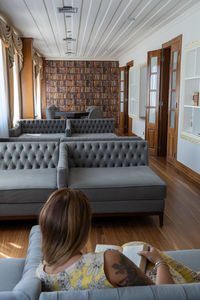 Rear view of woman sitting on sofa at home reading a book 