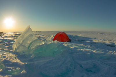 Tent on frozen landscape against sky during sunset