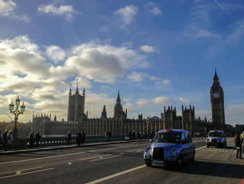 Cars on road in city against cloudy sky