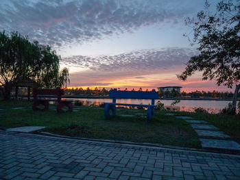 Footpath by lake against sky during sunset