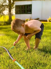 Shirtless boy playing with garden hose in yard