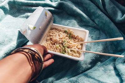 Midsection of person holding instant noodles yakisoba on light blue blanket at home