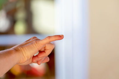 Cropped hand of man gesturing against window