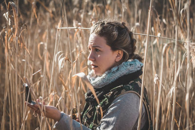 Side view of woman holding navigational compass while standing amidst plants