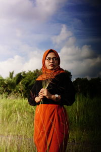 Portrait of young woman standing on field against sky