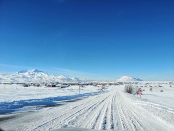 Snow covered road by mountain against blue sky