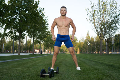 Portrait of shirtless man exercising on field