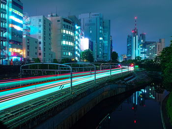 Light trails on city street by buildings against sky at night