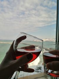 Close-up of hand holding wine glass against sky