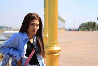 Portrait of smiling woman standing by pole against sky